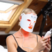 A woman wearing a white Block Blue Light red light therapy face mask with blue polka dots, holding a white controller.