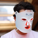 A person wearing a Block Blue Light red light-therapy face mask in a warm indoor setting.